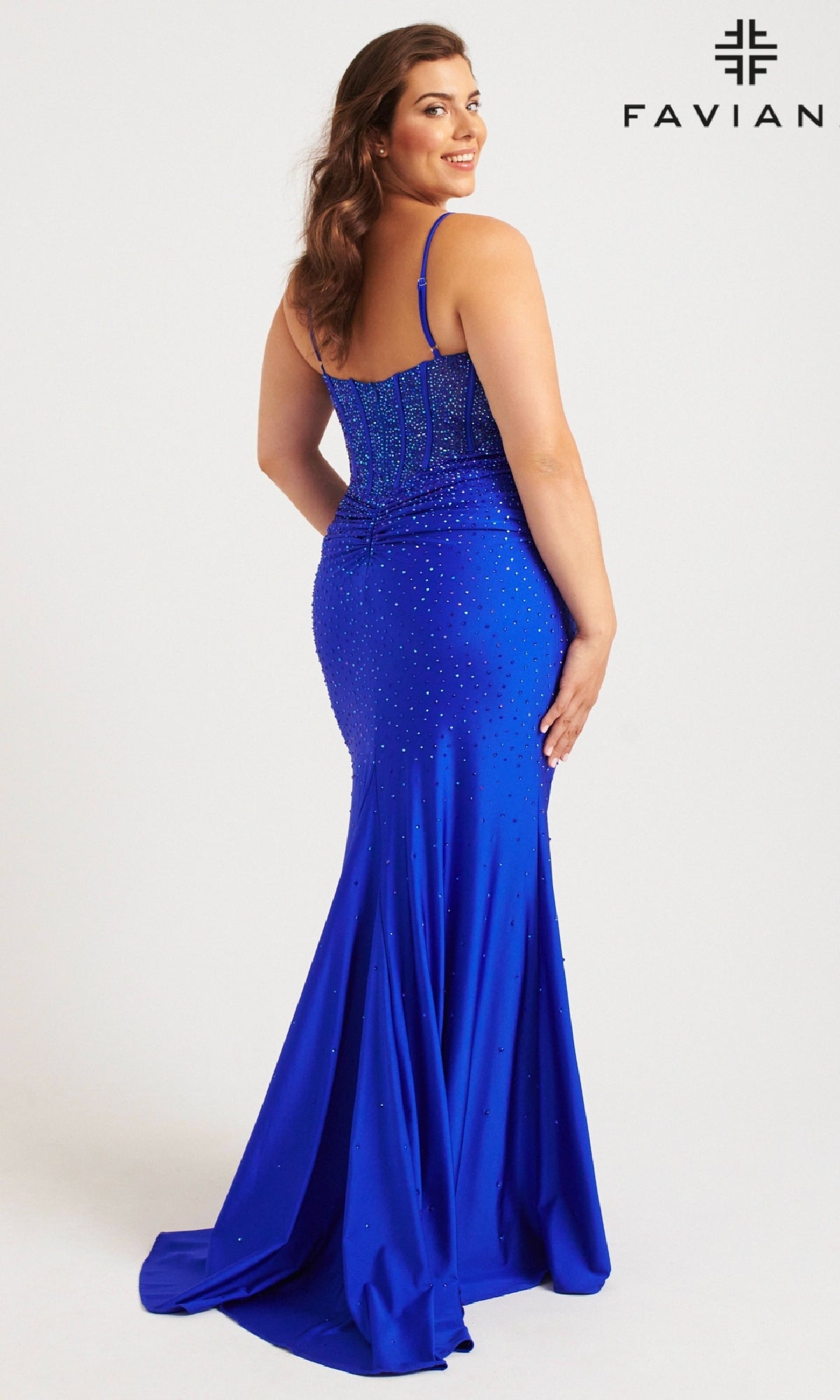 A woman wearing the Faviana 9555 Long Plus-Size Prom Dress in blue, featuring beads, a corset bodice, thin straps, and a fitted silhouette with a slight train, faces away from the camera. The Faviana logo appears in the top right corner.